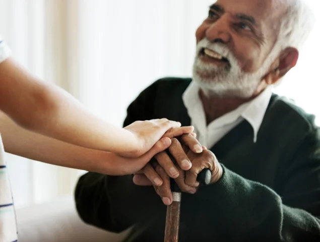 smiling, seated senior man rests his hands and looks up at his caregiver