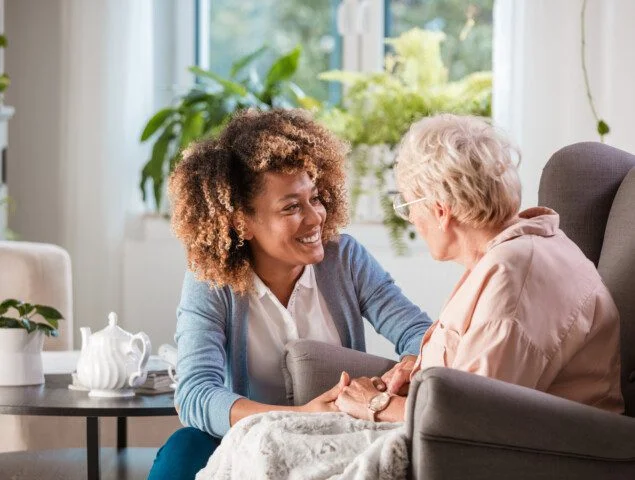 young woman smiling at older woman sitting in chair