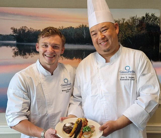 two smiling male chefs present a beautifully plated dish