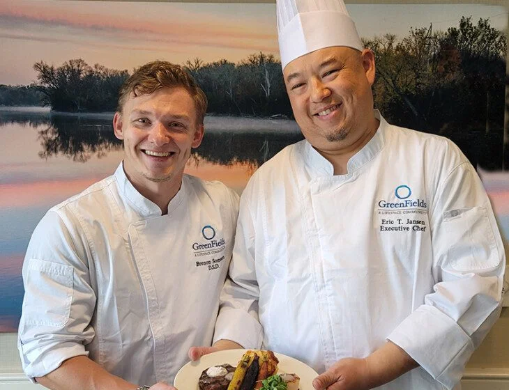 two smiling male chefs present a beautifully plated dish