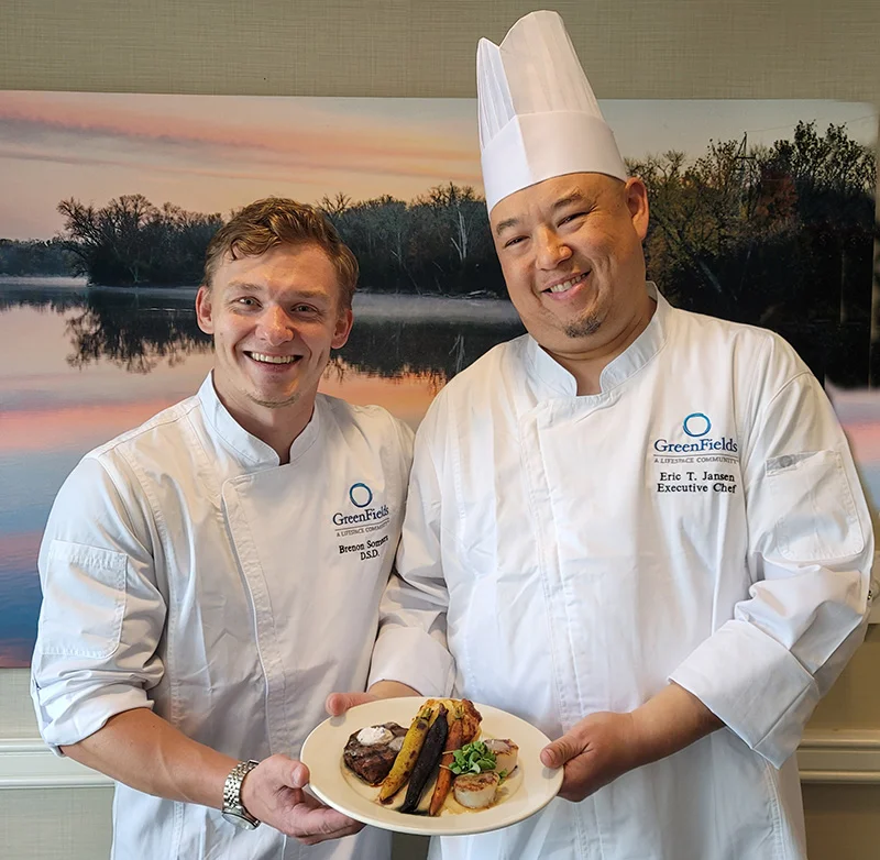 two smiling male chefs present a beautifully plated dish