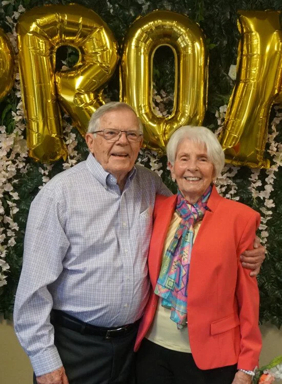 senior couple smiling and posed in front of a balloon sign reading "prom"
