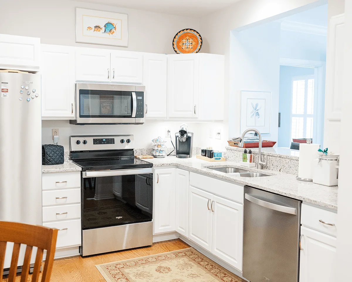 A bright kitchen with white cabinets, stainless steel appliances, and light-colored countertops.