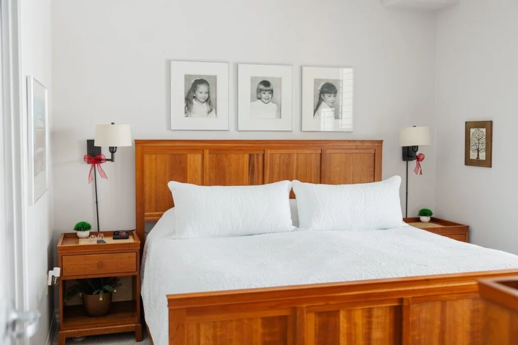 Bedroom in a GreenFields of Geneva apartment with a cherry wood bed, wall sconces, and framed family portraits.