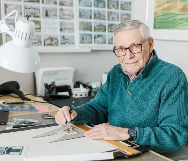 A resident draws at his drafting table beside his watercolor series of historic Geneva, Illinois houses.