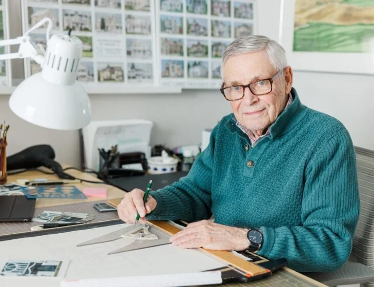 A resident draws at his drafting table beside his watercolor series of historic Geneva, Illinois houses.