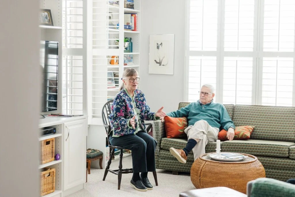 Two residents talking in the sunlit living room of their apartment at GreenFields of Geneva.
