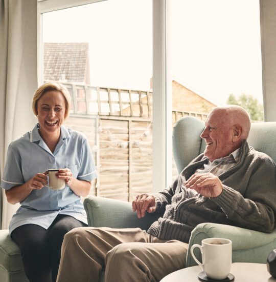 Indoor shot of smiling senior man and female enjoying coffee in living room