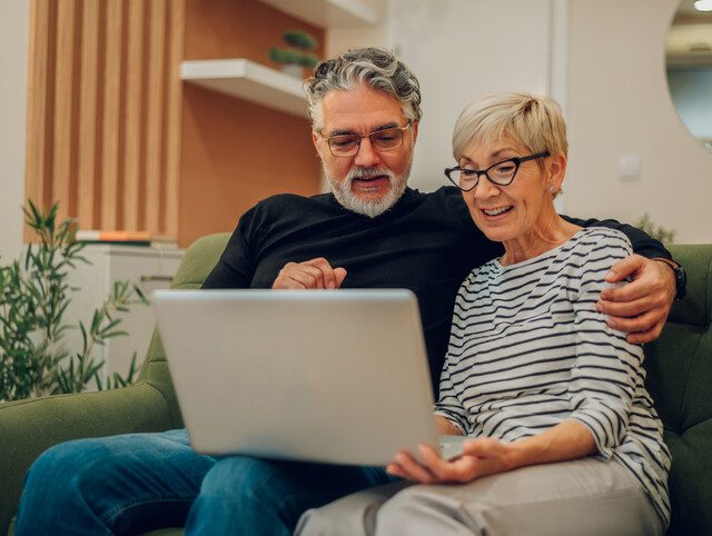 Older adult couple sitting on a couch using a laptop
