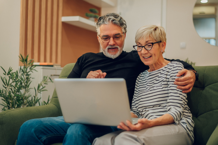 Older adult couple sitting on a couch using a laptop