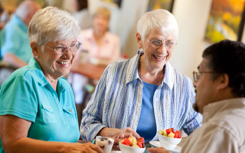 three senior friends converse while enjoying dessert