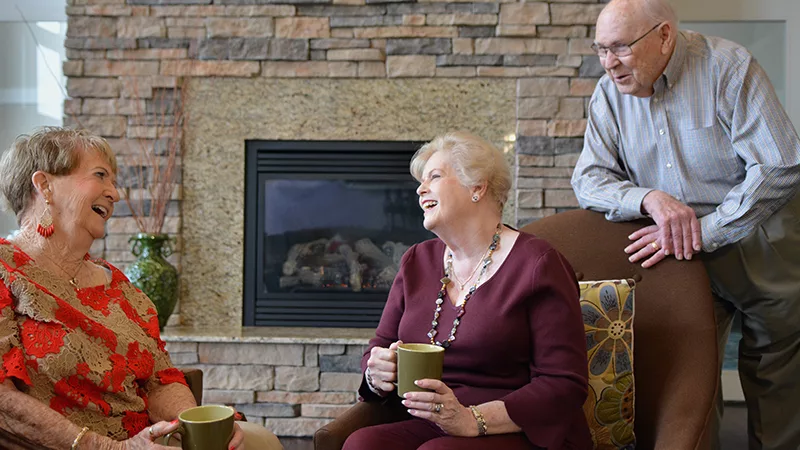 three senior friends conversing by a fireplace